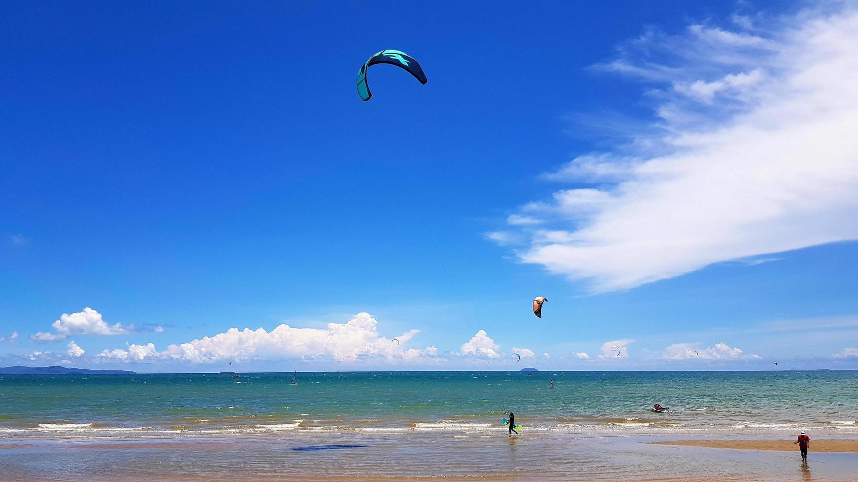 Many people playing kite, parasail or parachute on beach with sea or ocean , blue sky and cloud background with copy space. Activity and sport  concept photo