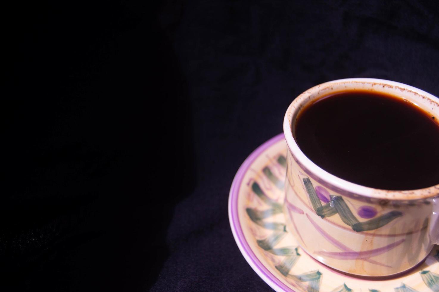 un vaso que contiene café negro preparado sobre un fondo negro foto