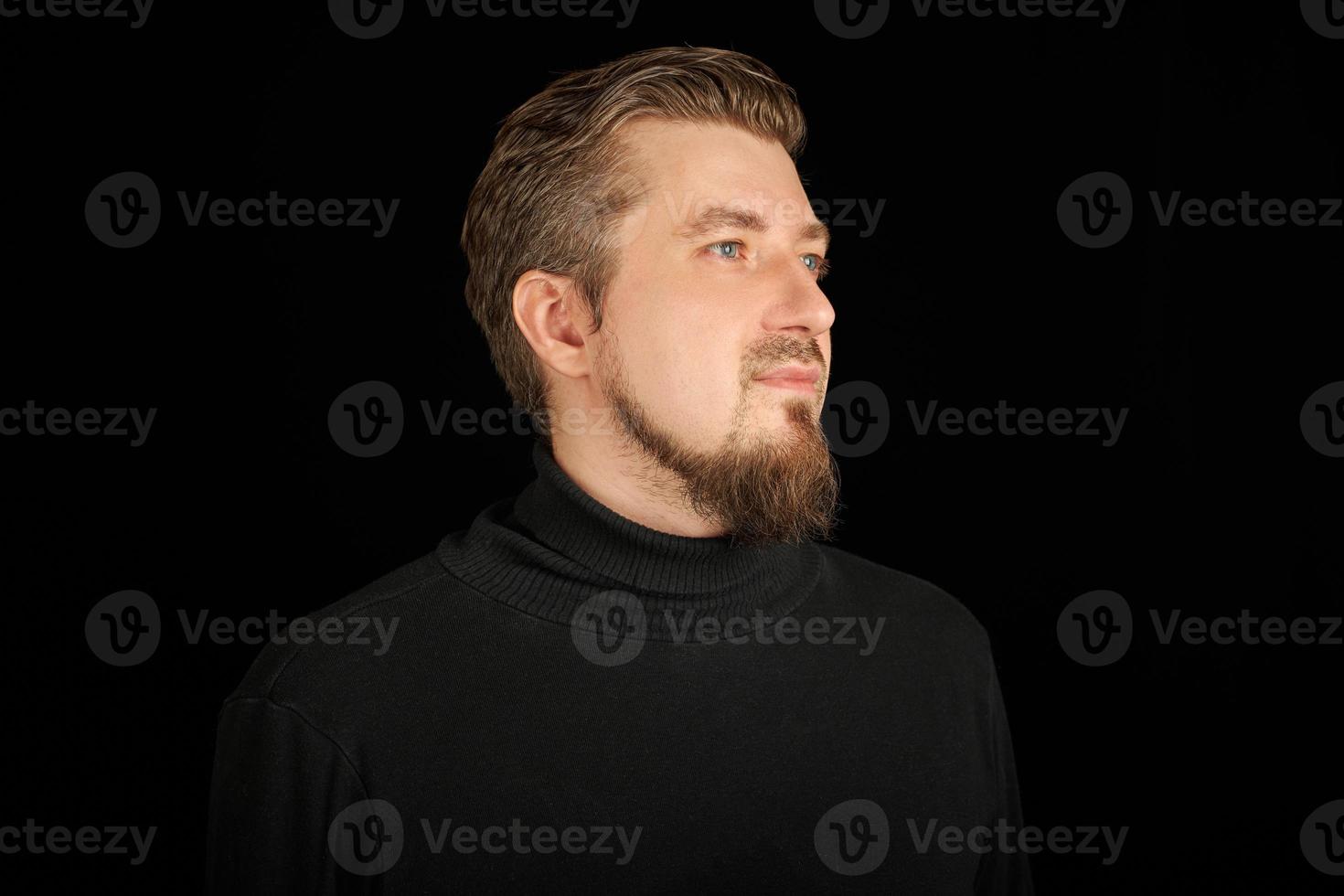 Cute bearded man, half-profile portrait, black background photo