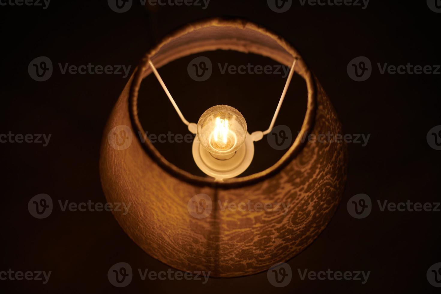 Incandescent lamp in round lampshade glowing in dark. photo