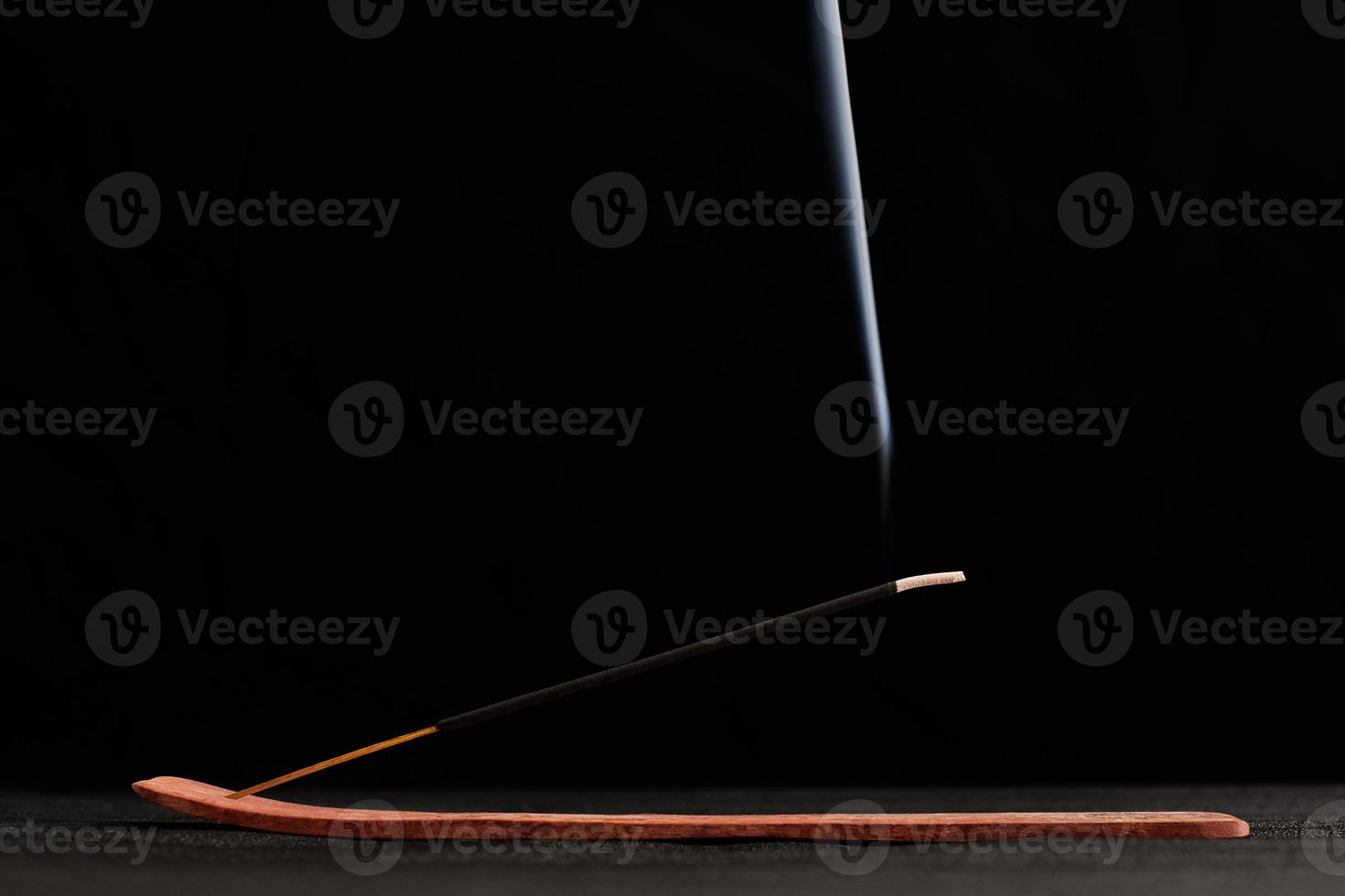 Smoke curls of burning incense stick in wooden holder for relaxation and meditation black background photo