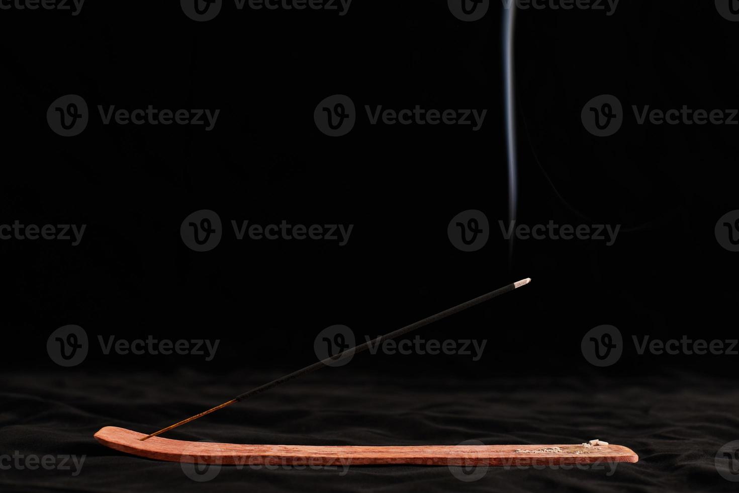 Smoke curls of burning incense stick in wooden holder for relaxation and meditation black background photo