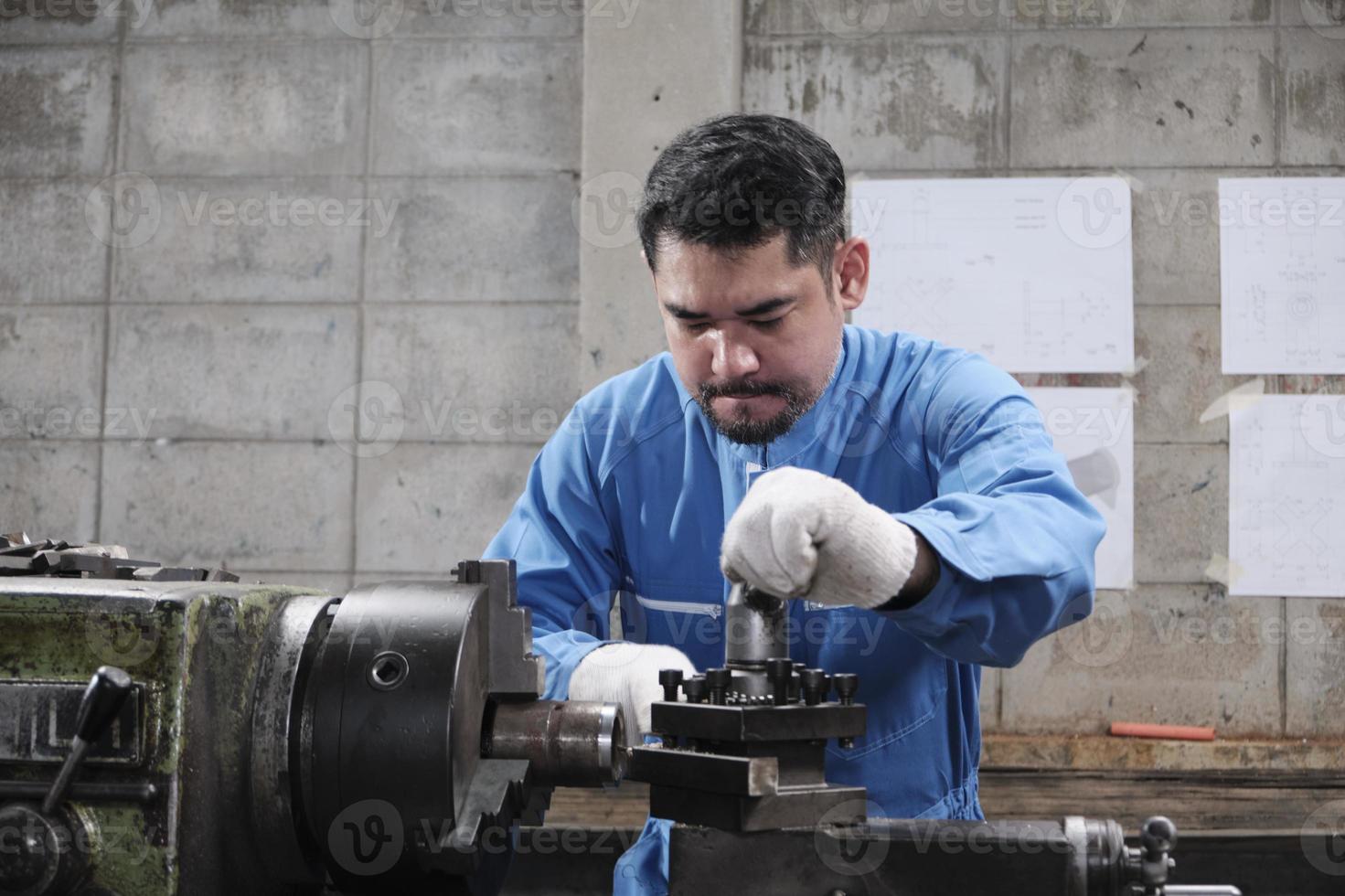 One professional Asian male industry engineer worker works in a safety uniform with metalwork precision tools, mechanical lathe machines, and spare parts workshop in the steel manufacturing factory. photo