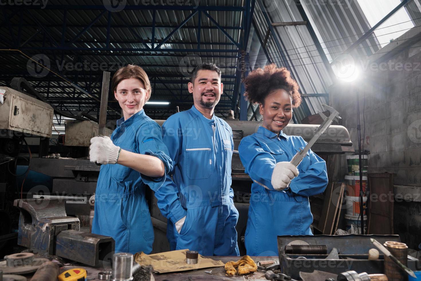 Multiracial industry workers in safety uniforms collaborate with unity, act with tools, and express happy work together with smile and cheerful in mechanical factory, professional engineer occupation. photo