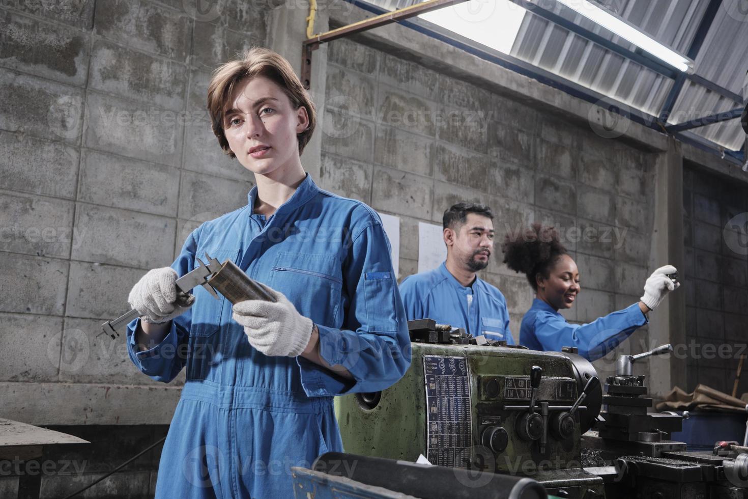 Young Caucasian female industry worker works with metalwork precision tools, lathe machines, and spare parts workshop with multiracial team in manufacturing factory, professional mechanical engineers. photo
