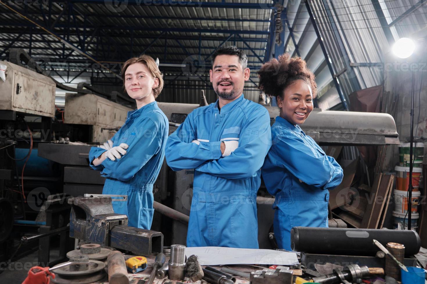 Multiracial industry workers in safety uniforms collaborate with unity, arms crossed, and express happy work together with smile and cheerful in mechanical factory, professional engineer occupation. photo