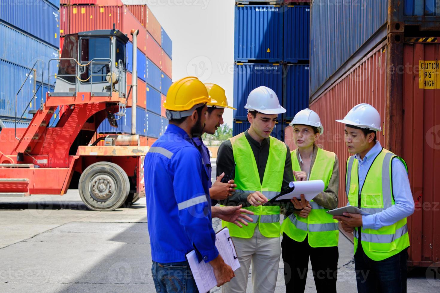 un grupo de trabajadores multirraciales con uniformes de seguridad y cascos trabajan en la terminal logística con muchas pilas de contenedores, control de carga y envío de mercancías para la industria del transporte de carga. foto