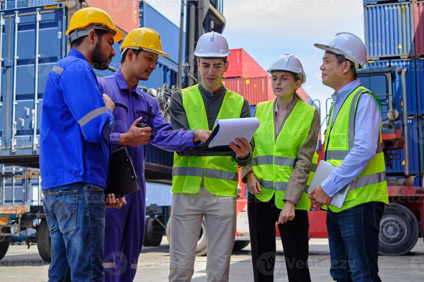 un grupo de trabajadores multirraciales con uniformes de seguridad y cascos trabajan en la terminal logística con muchas pilas de contenedores, control de carga y envío de mercancías para la industria del transporte de carga. foto