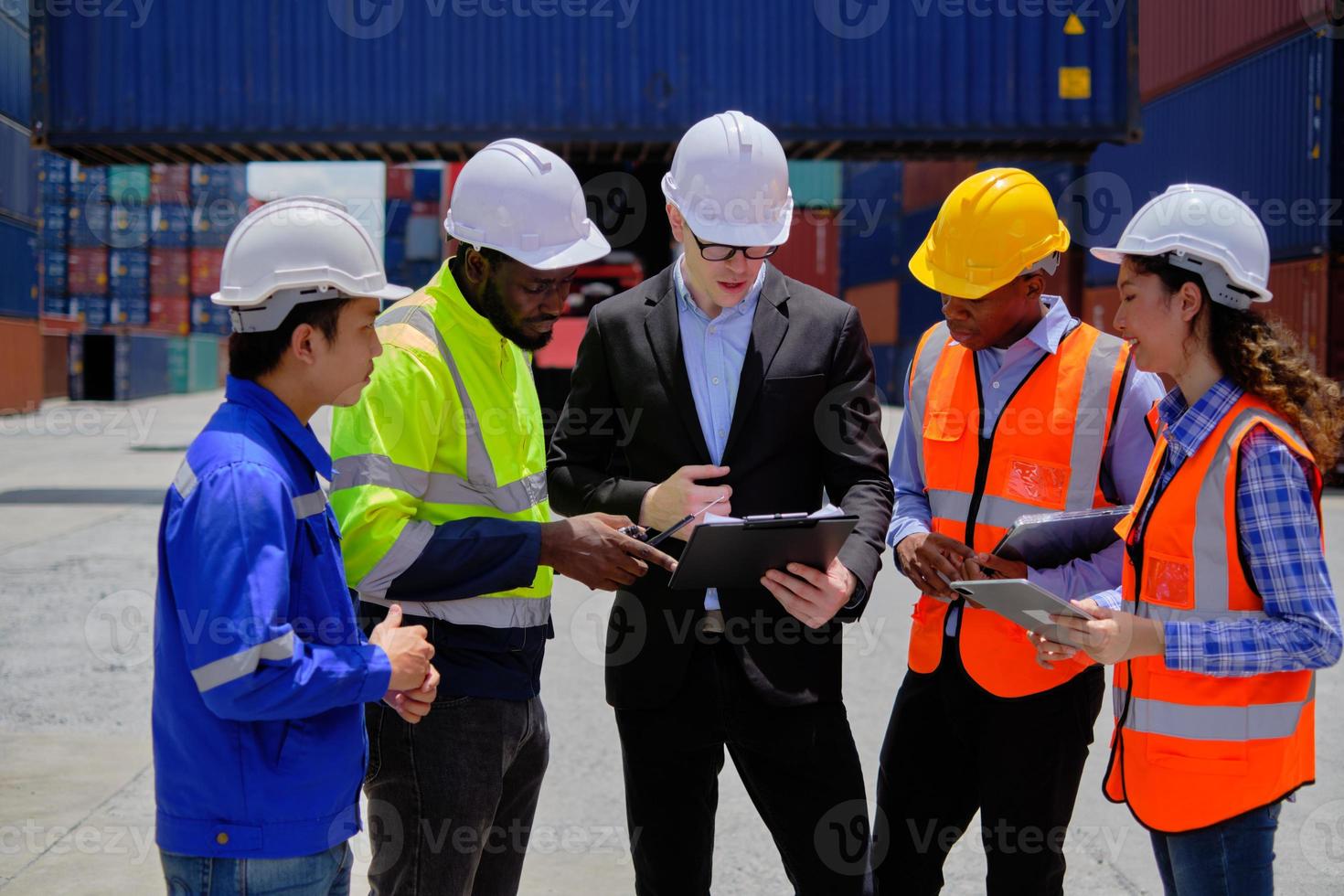 Group of multiracial workers in safety uniforms and hardhats work at logistics terminal dock with stacks of containers, loading control, and management shipping goods, cargo transportation industry. photo