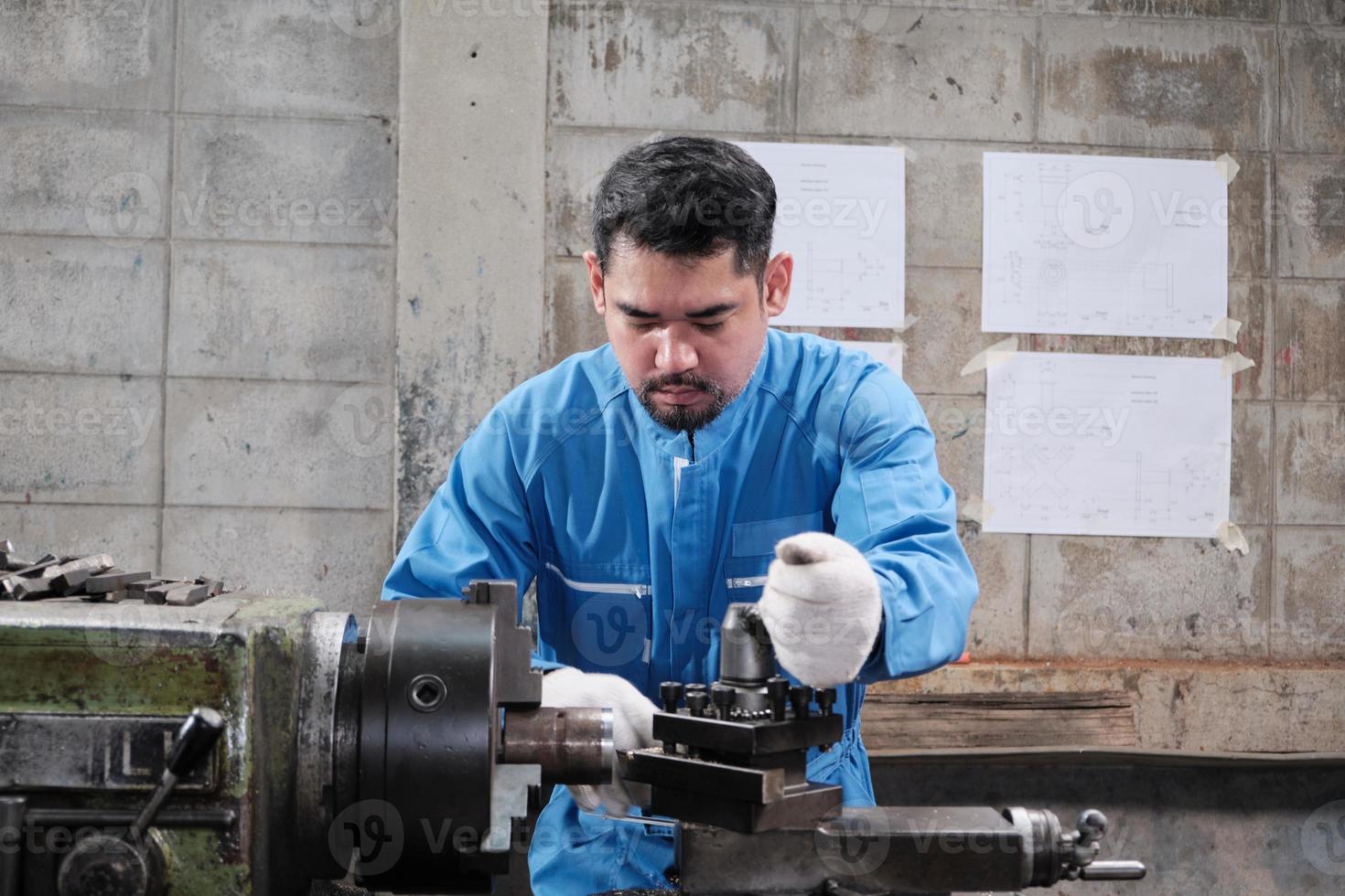 One professional Asian male industry engineer worker works in a safety uniform with metalwork precision tools, mechanical lathe machines, and spare parts workshop in the steel manufacturing factory. photo