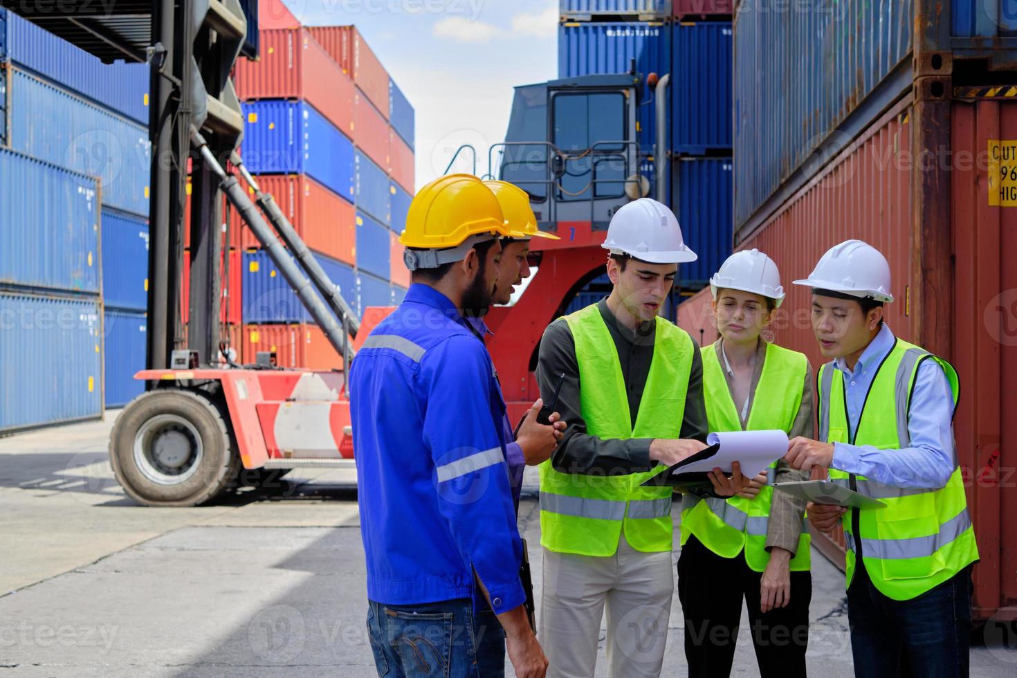 un grupo de trabajadores multirraciales con uniformes de seguridad y cascos trabajan en la terminal logística con muchas pilas de contenedores, control de carga y envío de mercancías para la industria del transporte de carga. foto