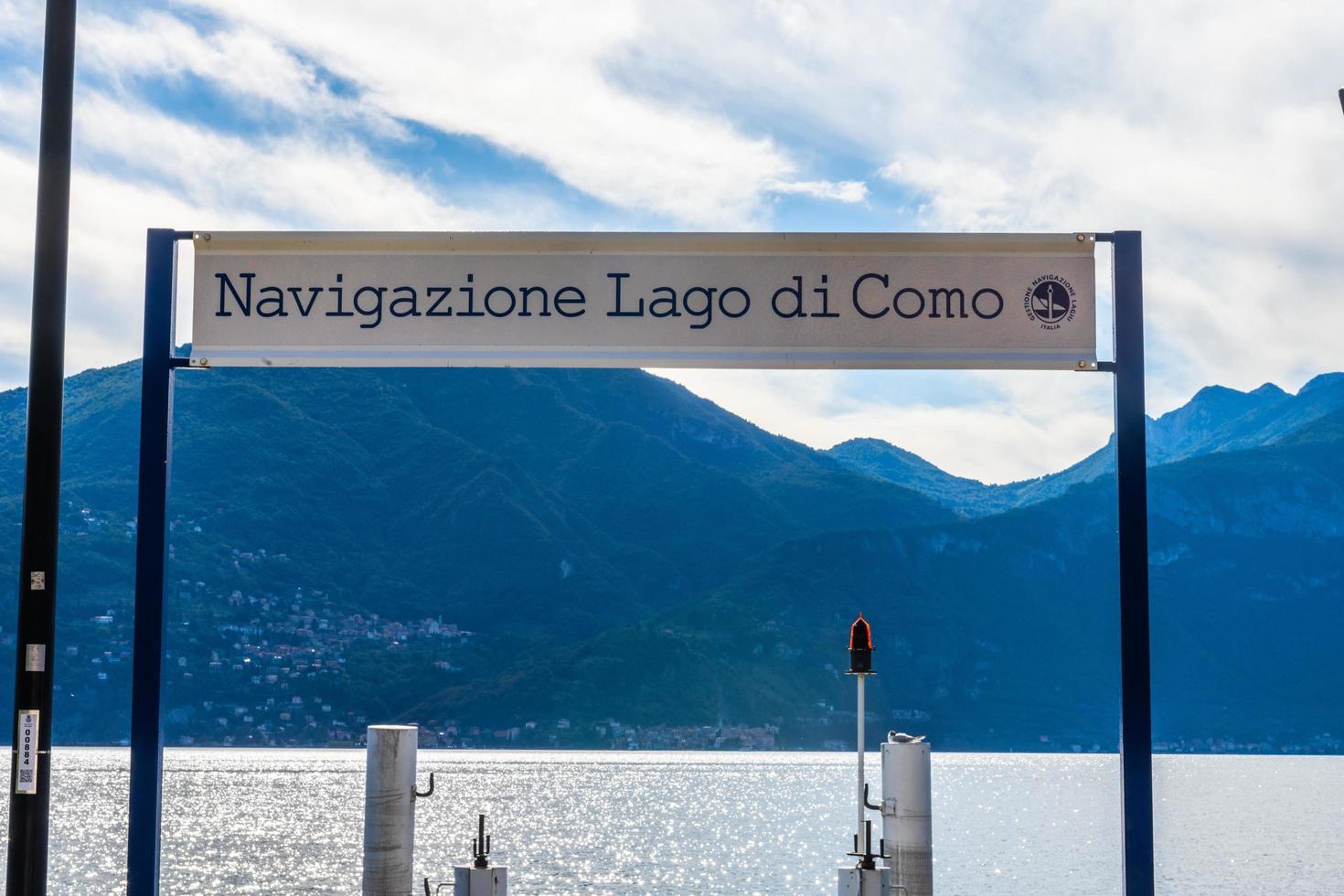 Fotografía de Stock del muelle del ferry y el signo del ferry, lago de Como, Lombardía, Italia. el cartel dice navigazione lago di como. este muelle está en menaggio. es un hermoso día soleado de verano foto