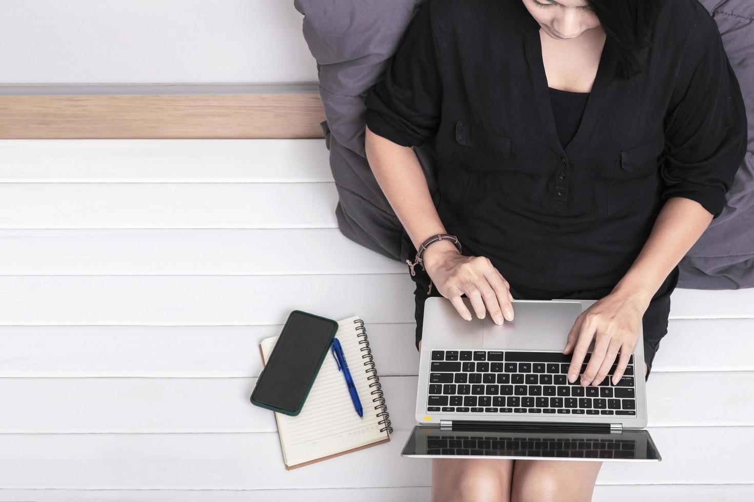 Top view of a young asian woman using laptop computer sitting on wooden floor at home , work from home concept photo