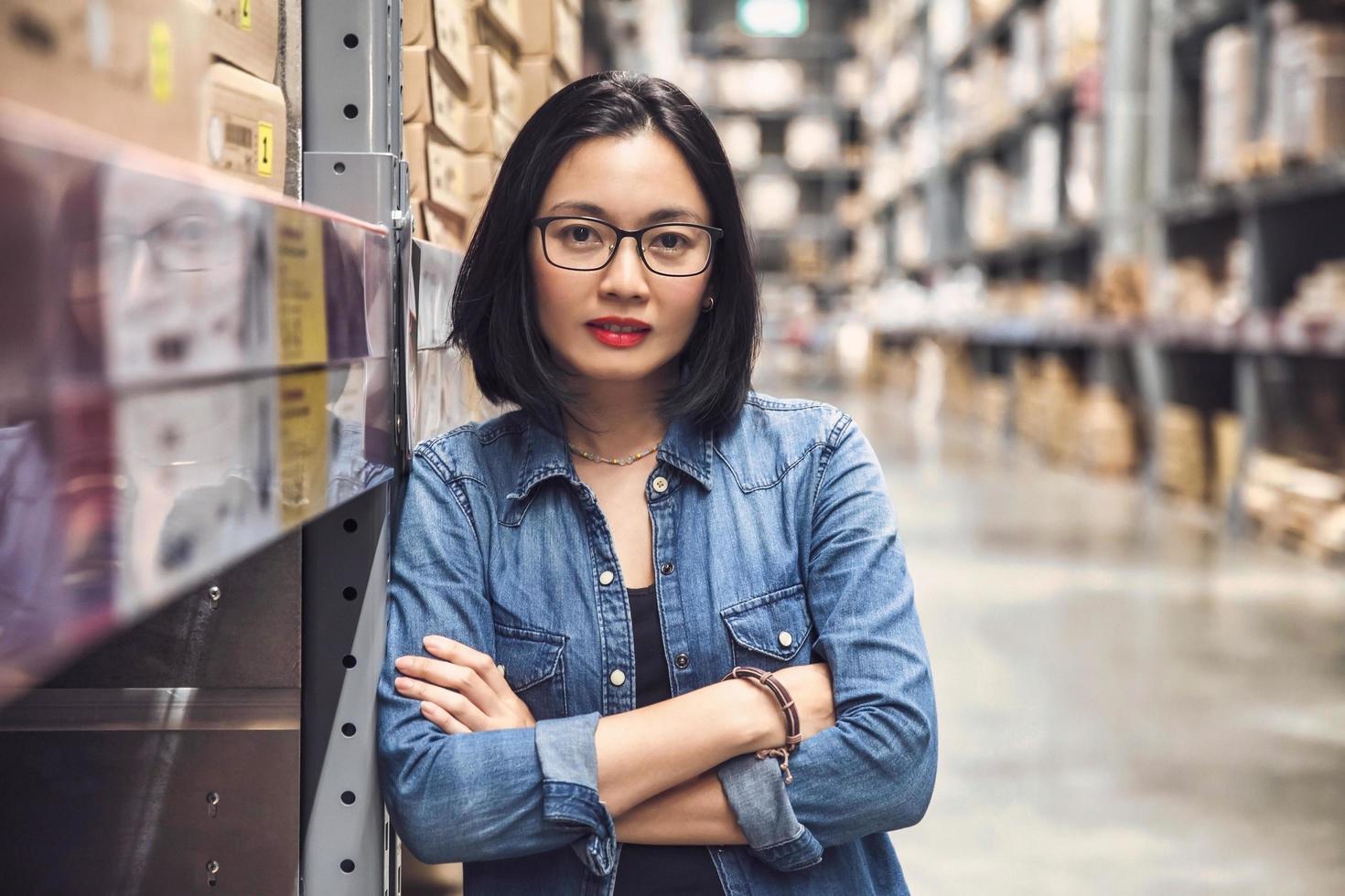 Asian beautiful young woman worker of furniture store with arms crossed in a large warehouse. photo