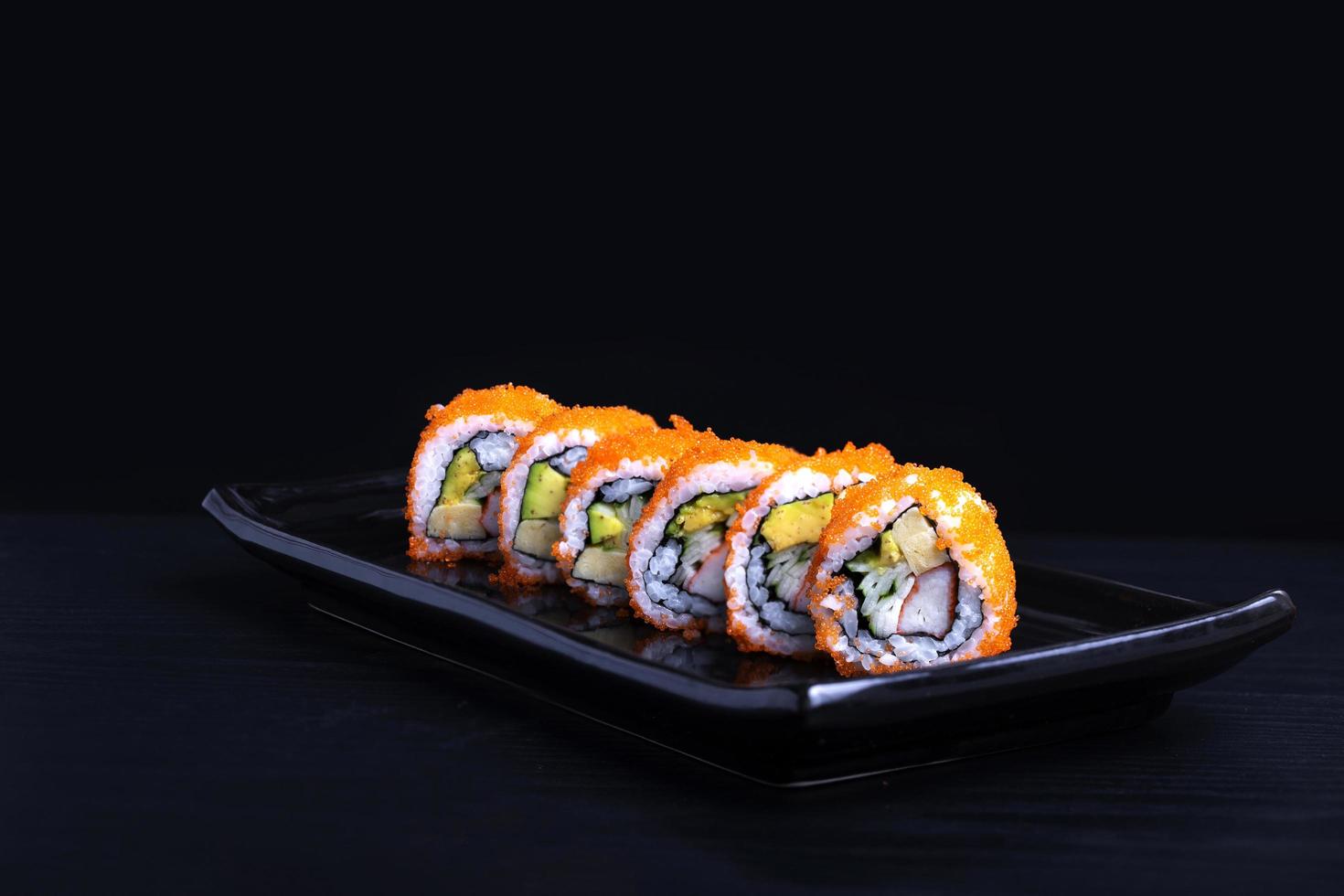 rollos maki de sushi seguidos con salmón, gambas, aguacate, queso crema aislado en fondo negro, menú de restaurante de comida japonesa foto