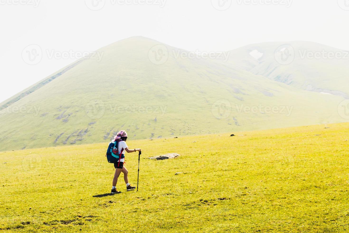 Side view fit sporty female hiker with nordic walk sticks go uphill in green hiking trail in caucasus mountains .Recreational activities and healthy lifestyle concept photo