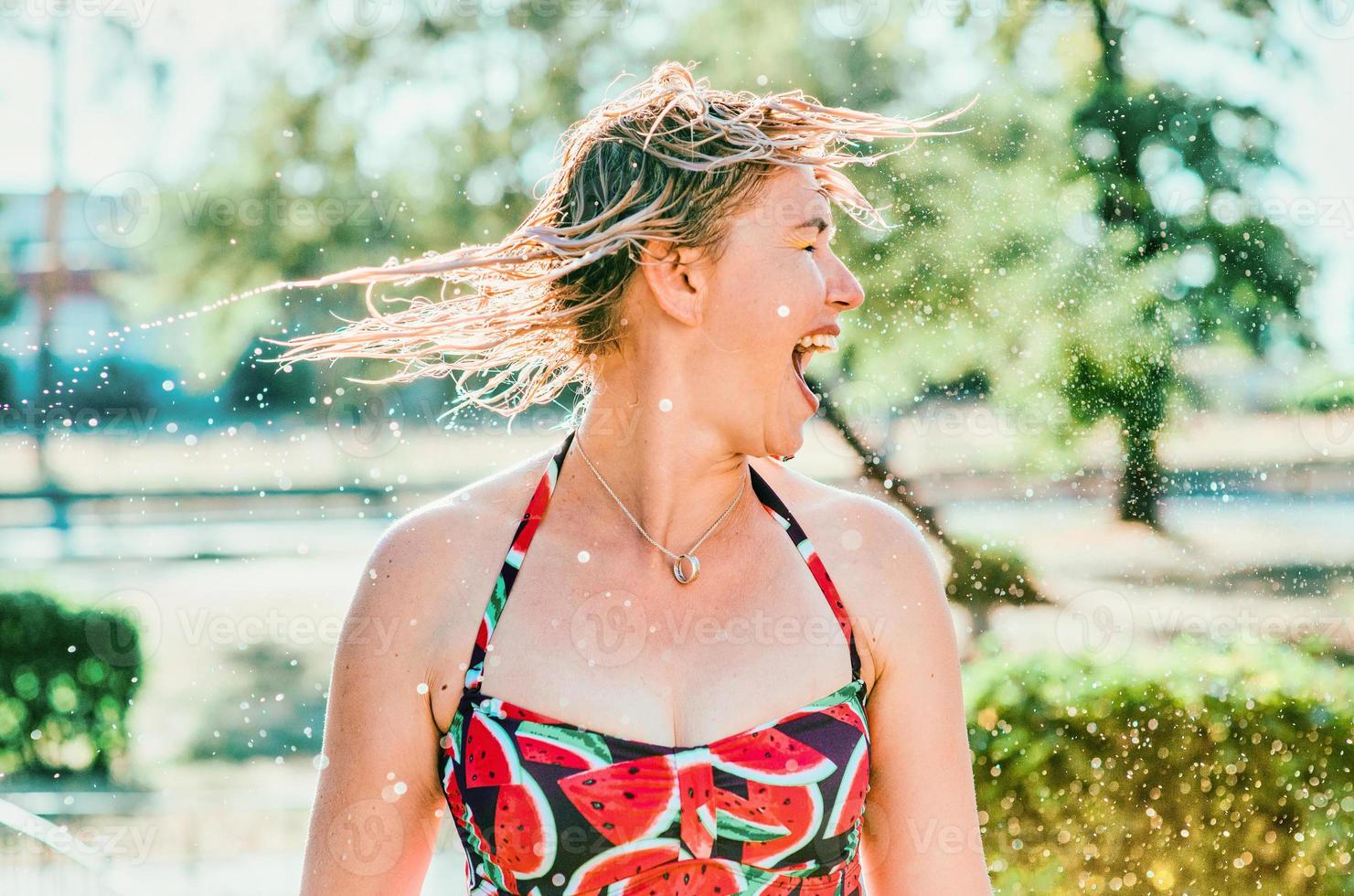 risa emocional mujer rubia con el pelo mojado haciendo salpicaduras de agua. vacaciones, felicidad, diversión, verano, concepto de ocio. foto