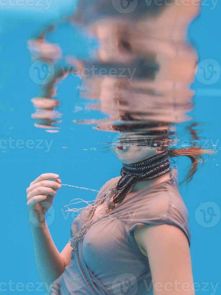 surreal art portrait of young woman in grey dress and beaded scarf underwater in the swimming pool photo