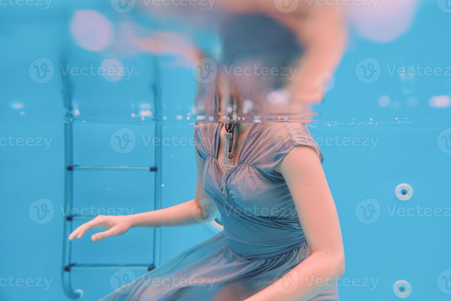 surreal art portrait of young woman in grey dress and beaded scarf underwater in the swimming pool photo