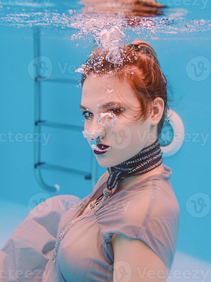 surreal art portrait of young woman in grey dress and beaded scarf underwater in the swimming pool photo