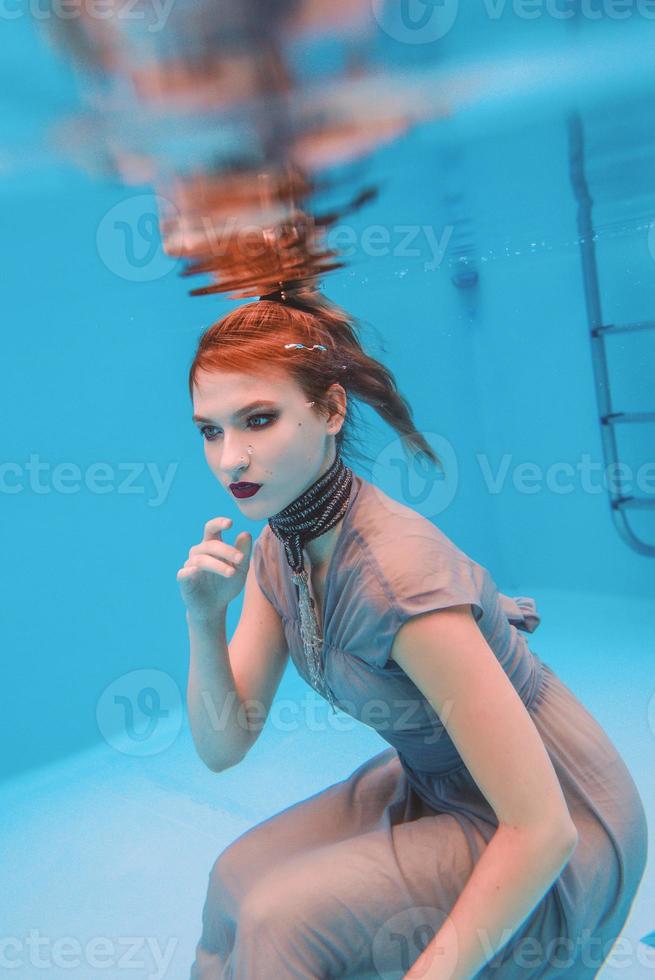 surreal art portrait of young woman in grey dress and beaded scarf underwater in the swimming pool photo