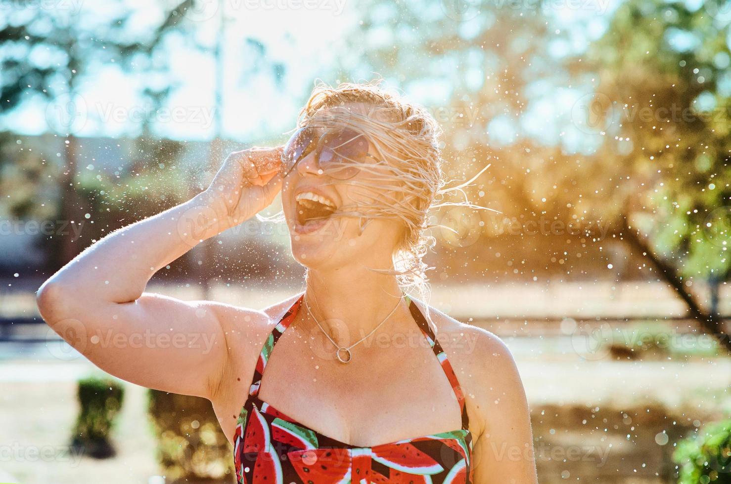 risa emocional mujer rubia con el pelo mojado haciendo salpicaduras de agua. vacaciones, felicidad, diversión, verano, concepto de ocio. foto