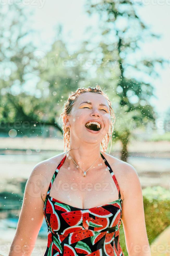 risa emocional mujer rubia con el pelo mojado haciendo salpicaduras de agua. vacaciones, felicidad, diversión, verano, concepto de ocio. foto