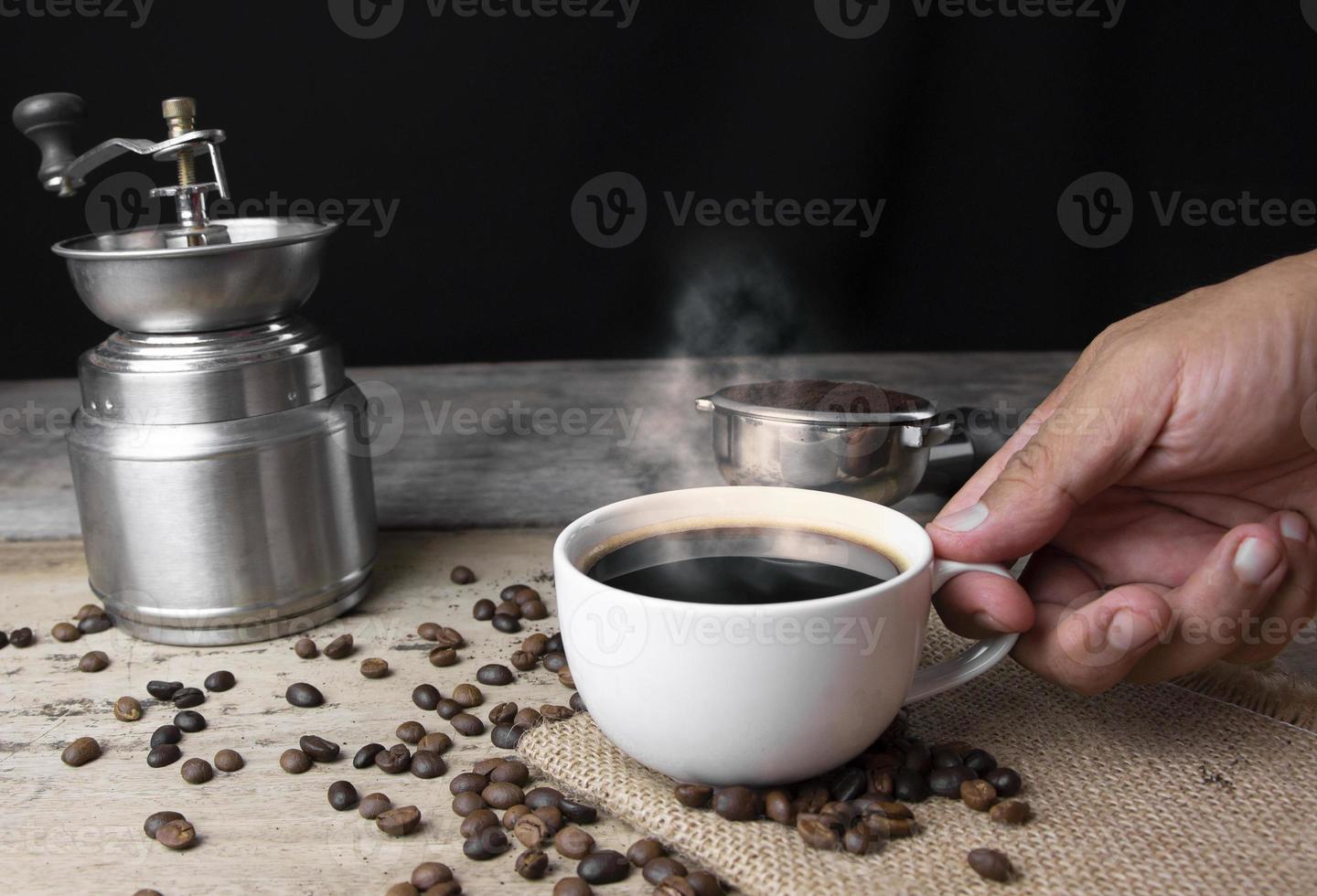 Front view hand holding cup of black Americano coffee on a wooden table with a pile of roasted Arabica coffee beans on black background. photo