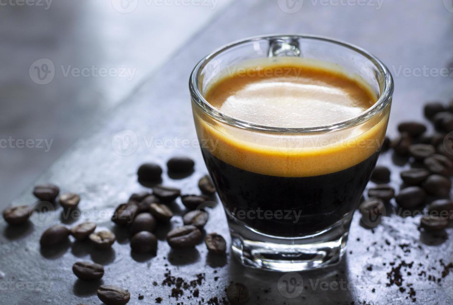 cup of hot espresso with a nice crema on a rustic concrete table with a pile of roasted arabica coffee. photo