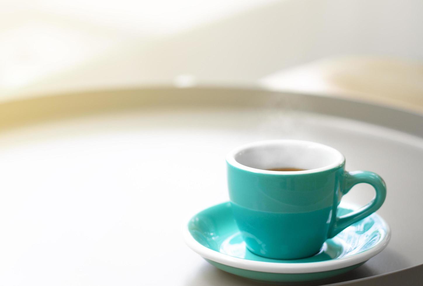 Cup of black hot coffee on a table in cafe with steam and morning sunlight. photo