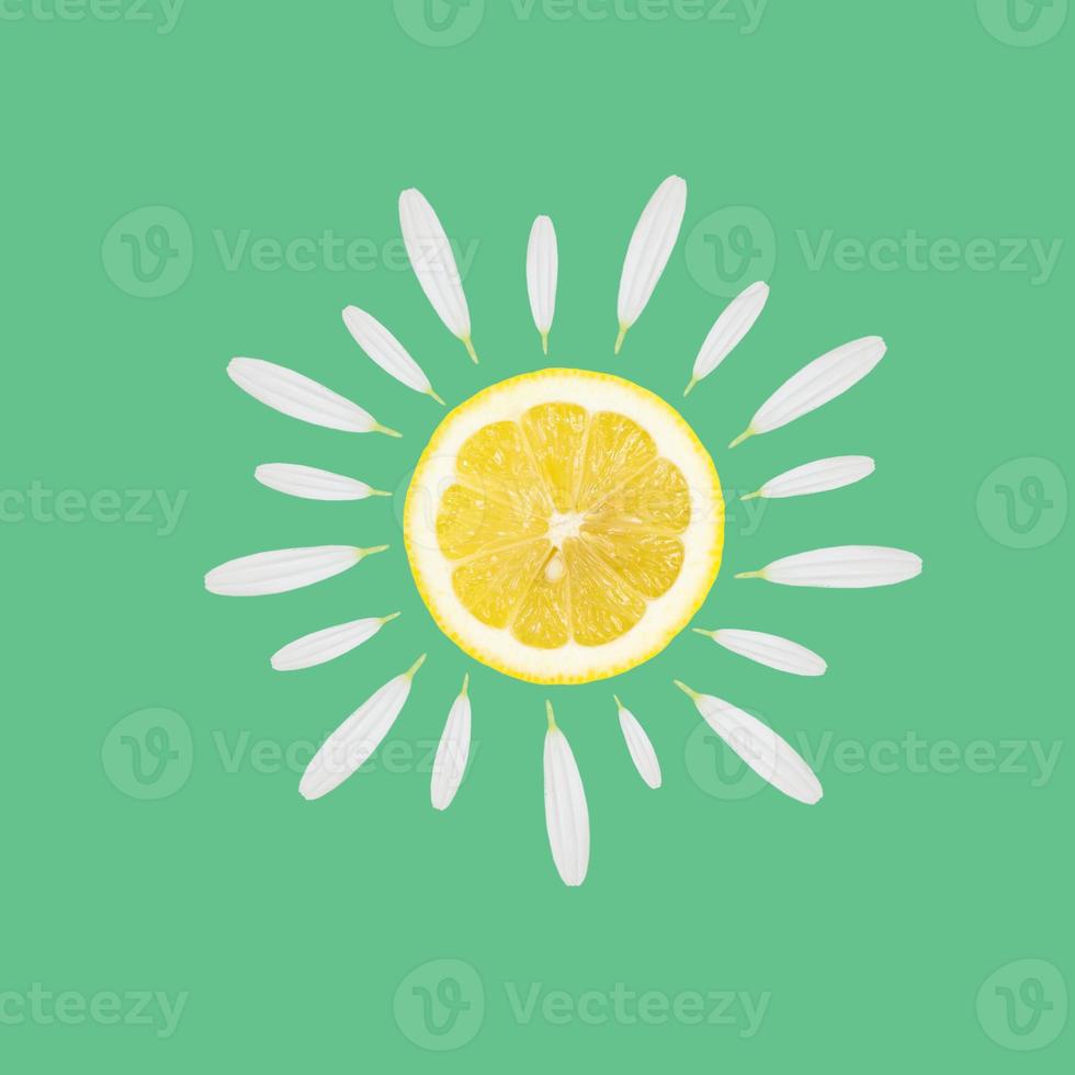 Ripe lemon slice with beautiful fresh chamomile flowers on light green background. Summer concept. photo