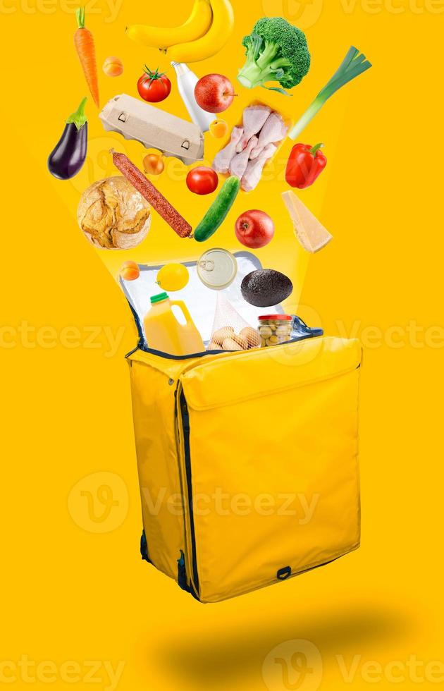 Vegetables, products that flying out of a open yellow courier food delivery bag, isolated on a yellow background. Food delivery concept. photo