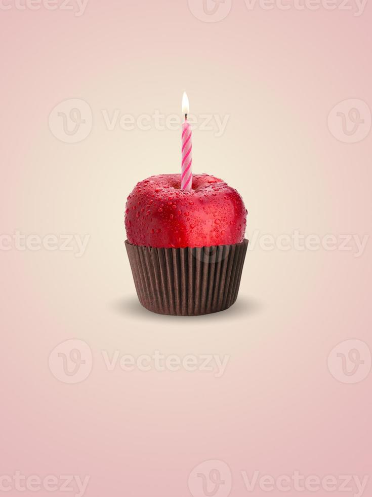 cupcake saludable de jugosa manzana roja con vela rosa sobre un fondo rosa. tarjeta de felicitación de fitness. concepto de dieta. foto