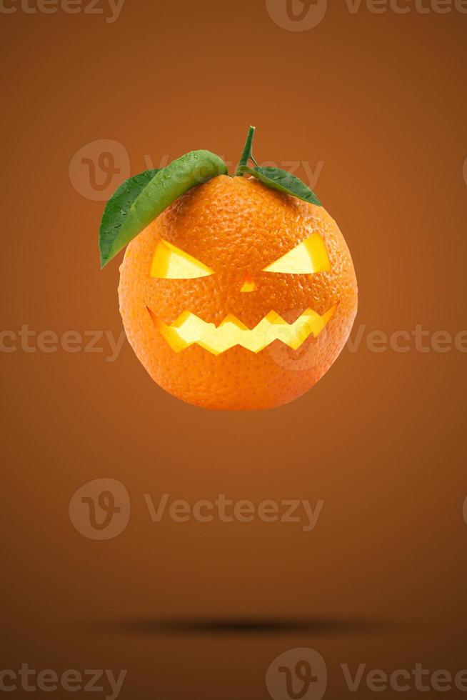 naranja fresca como cabeza de calabaza volando sobre fondo naranja pastel. concepto creativo de vacaciones feliz halloween. tarjeta de felicitación de la fiesta de halloween. concepto de temporada mínima. foto