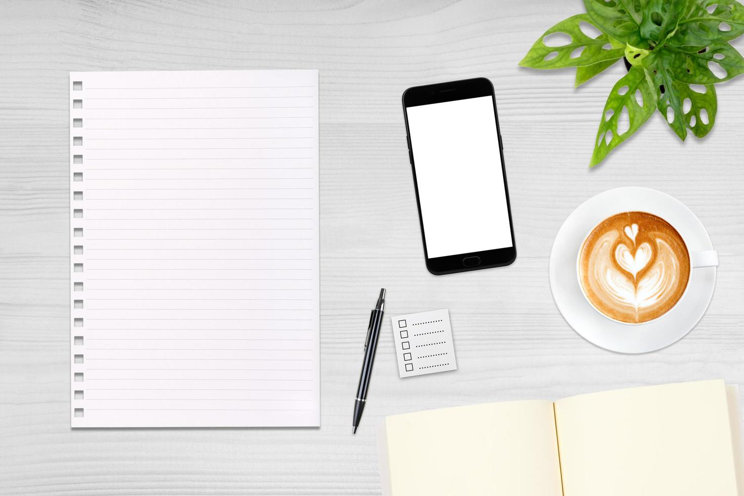 An open blank notebook, smartphone with pen and a cup of latte coffee on wooden table. photo