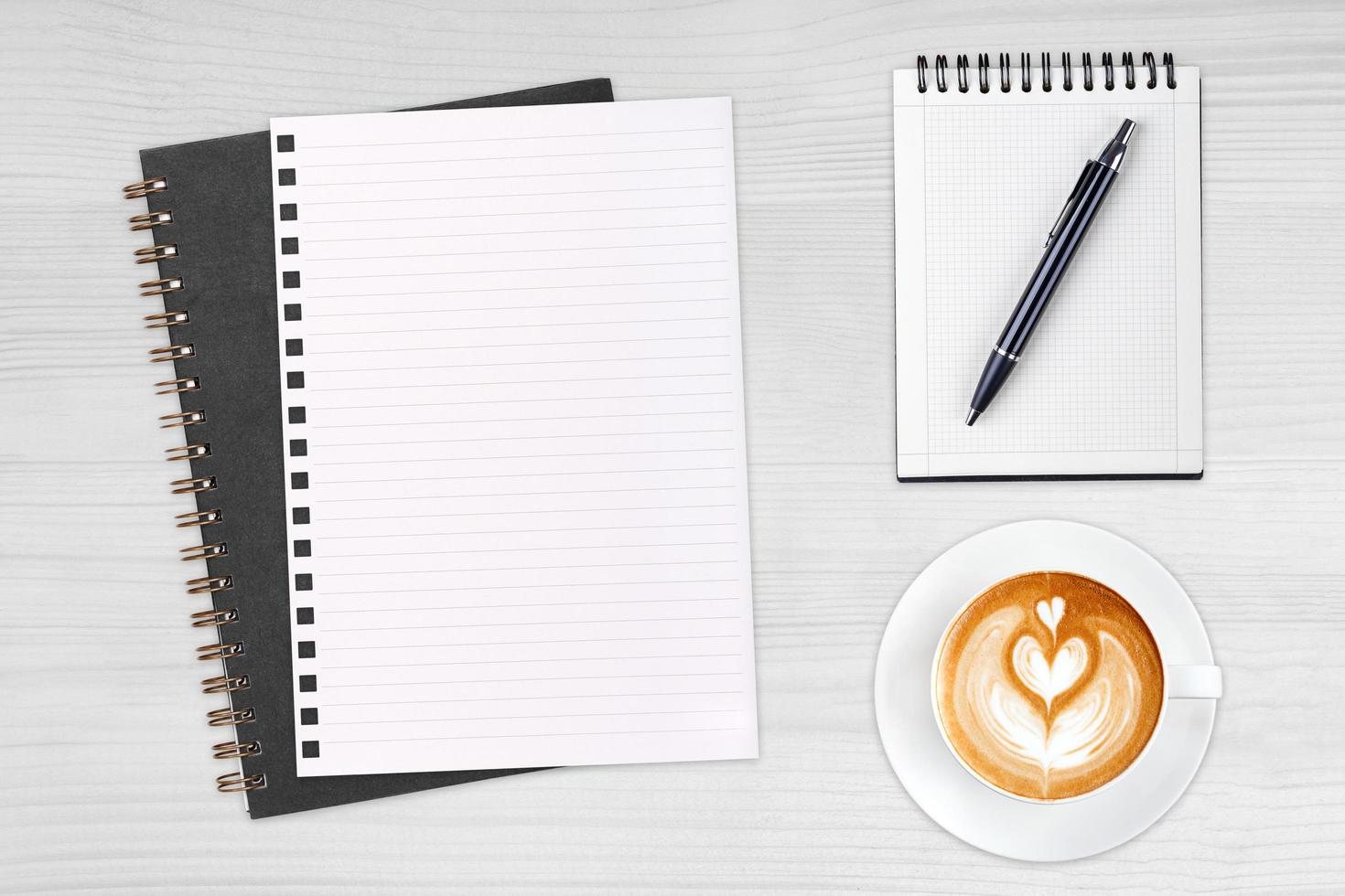 An open blank notebook with pencil and a cup of coffee on wooden table. Latte art coffee on top photo