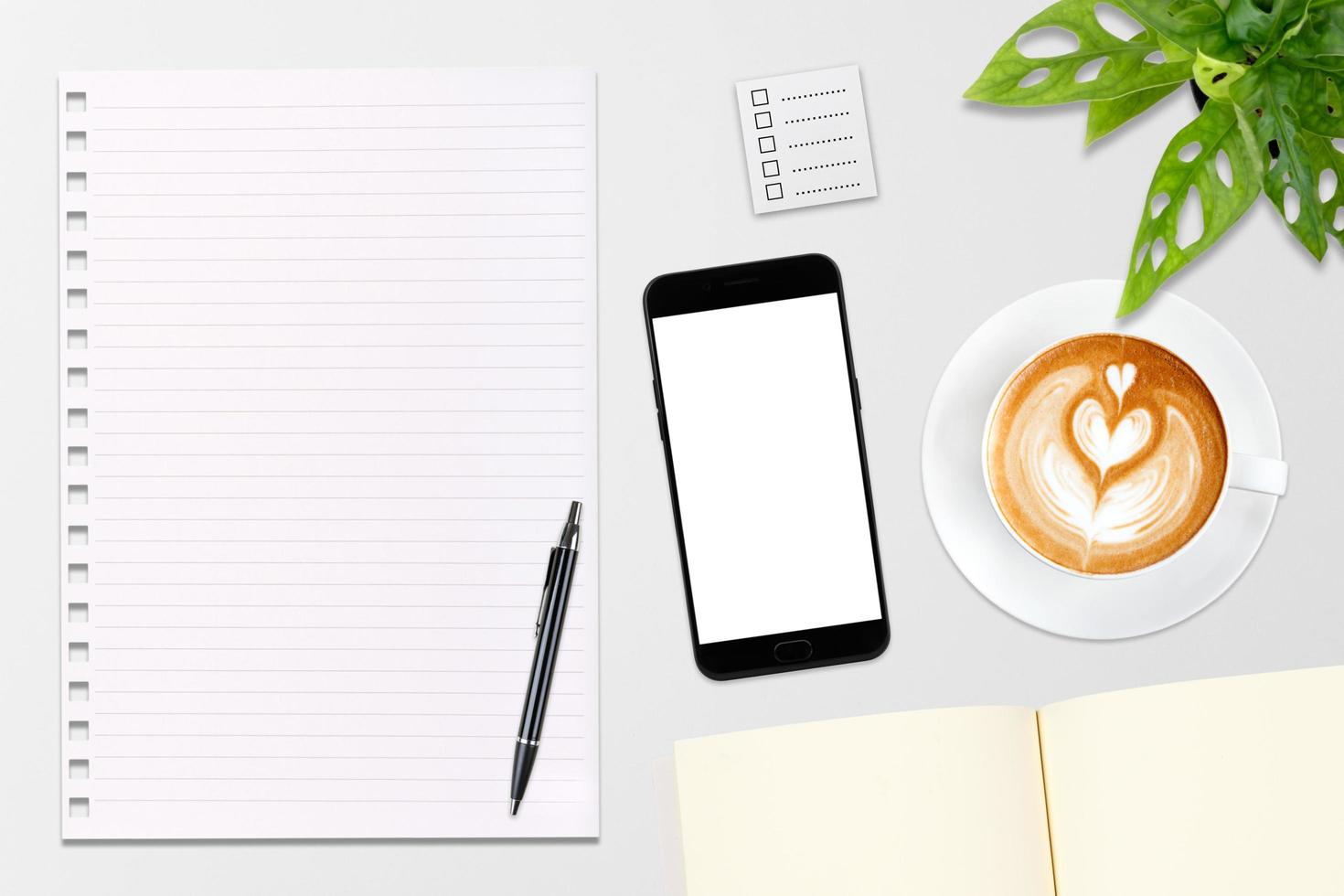 un cuaderno en blanco abierto, un teléfono inteligente con bolígrafo y una taza de café con leche en una mesa de madera. foto