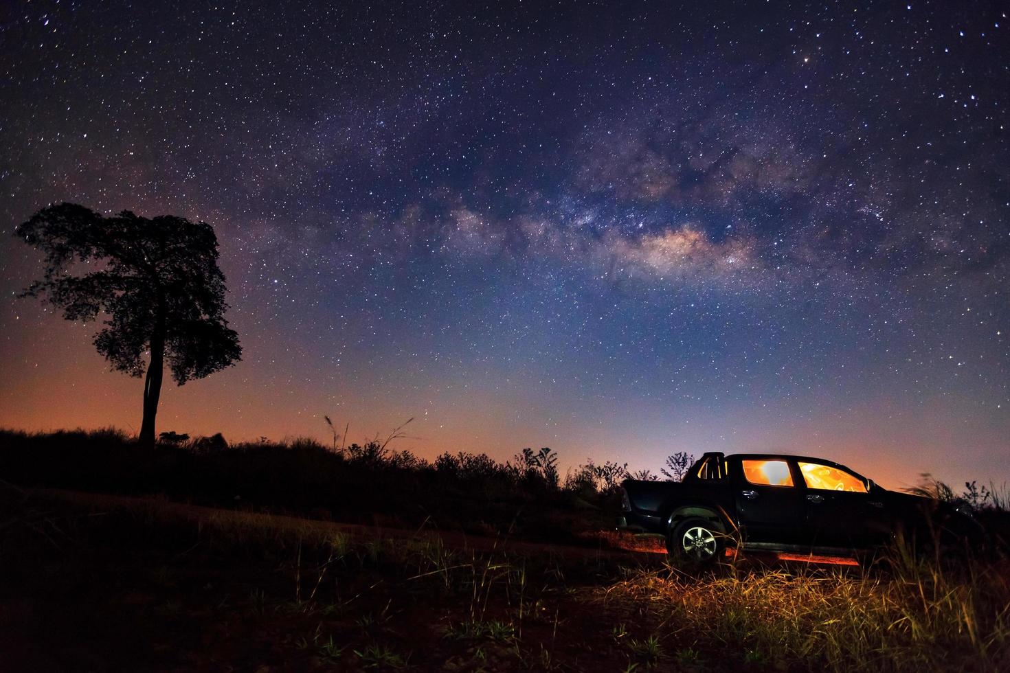 Night landscape on field with car and Milky Way. Long exposure photograph.with grain photo