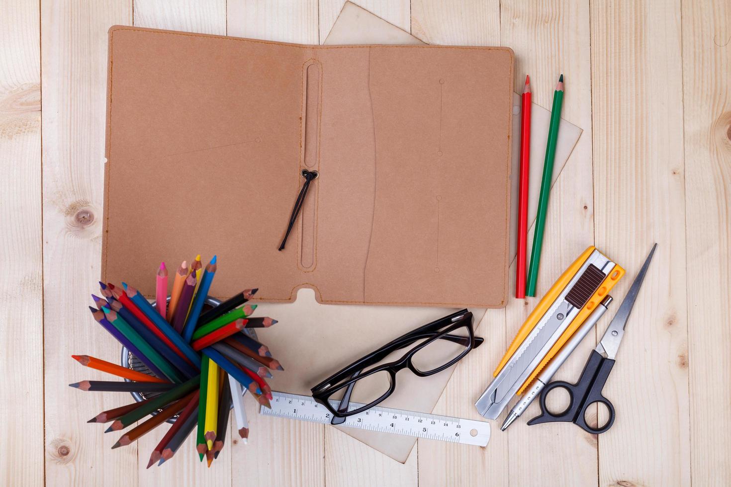 Workplace with colored pencils and supplies, notebook, eyeglass on wooden table photo