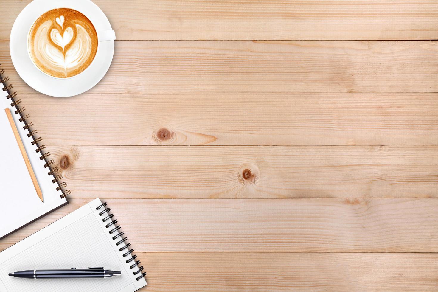 An open blank notebook with pencil and a cup of coffee on wooden table. Latte art coffee on top photo