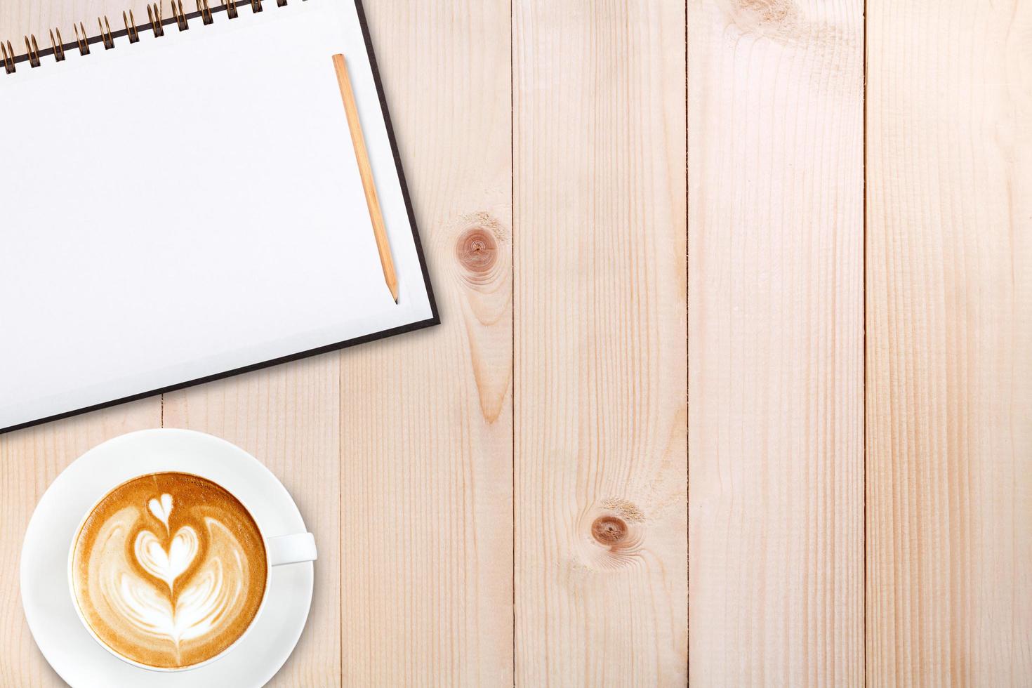 An open blank notebook with pencil and a cup of coffee on wooden table. Latte art coffee on top photo