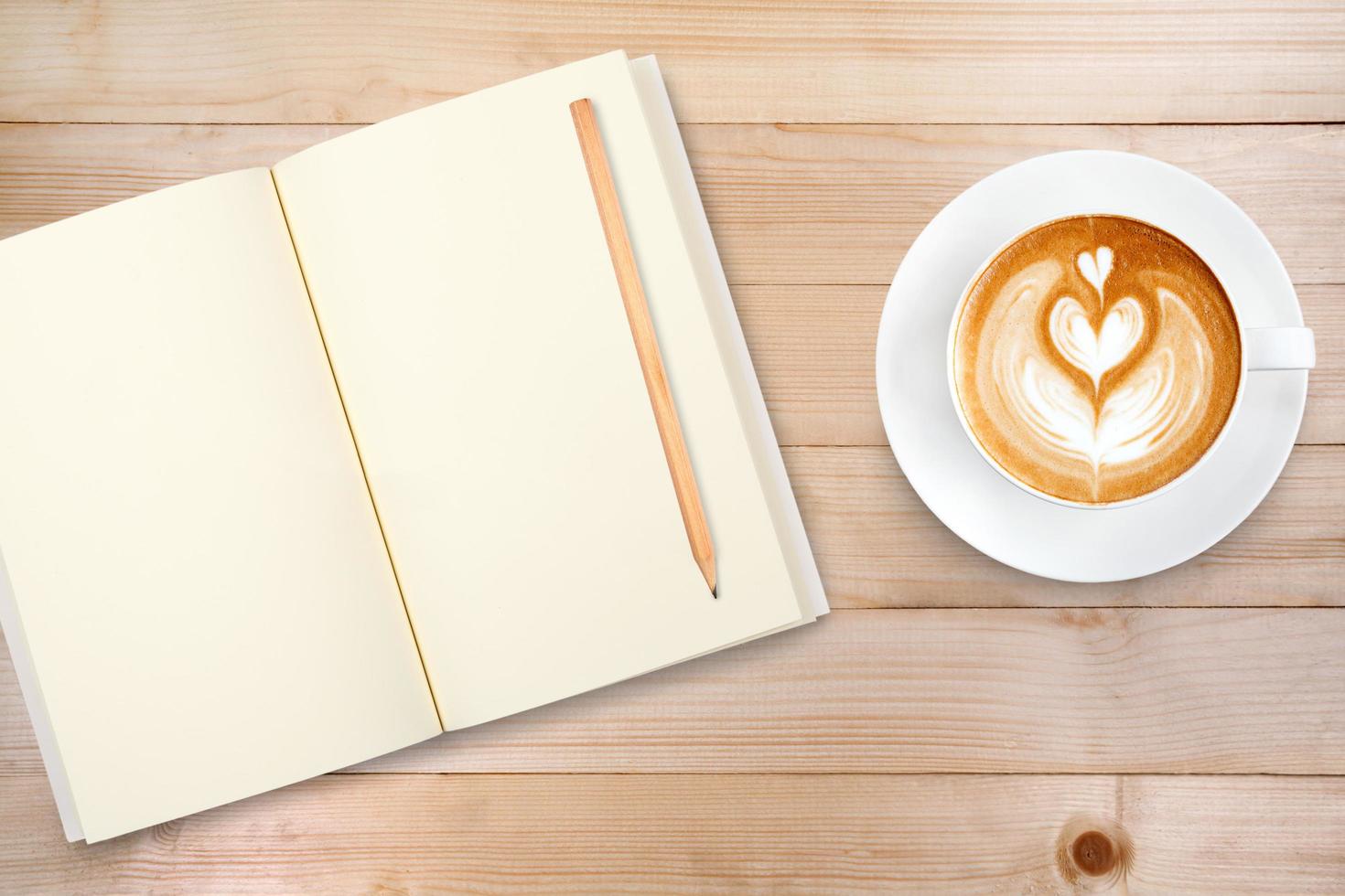 An open notebook with pencil and a cup of coffee on wooden table. Latte art coffee on top photo