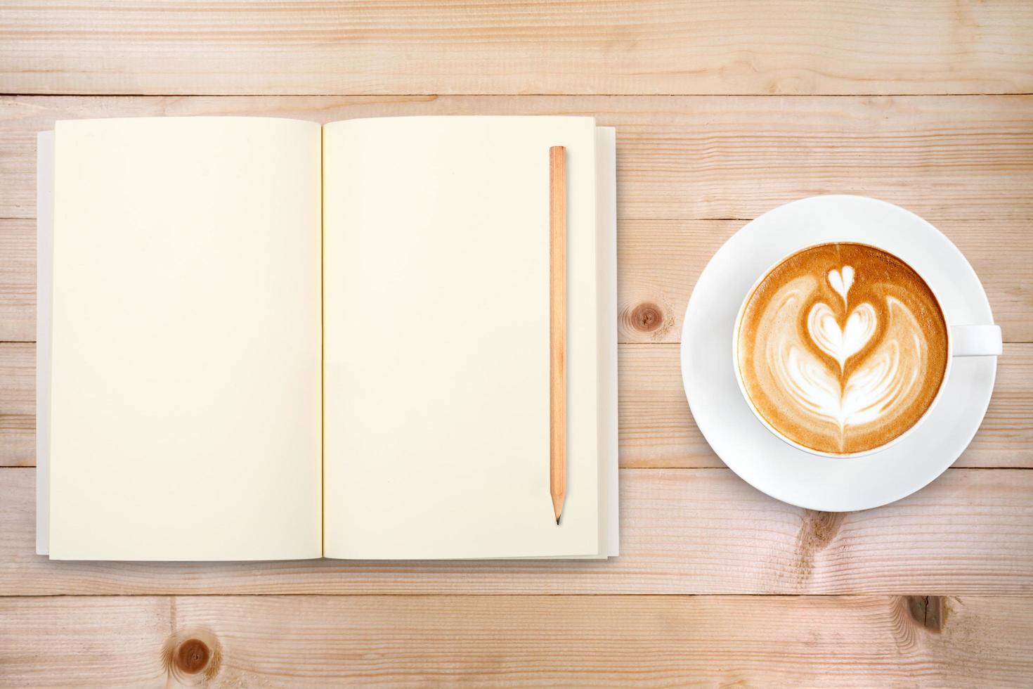 An open notebook with pencil and a cup of coffee on wooden table. Latte art coffee on top photo