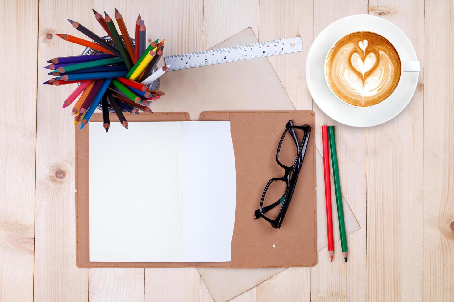 An open blank notebook with colour pencils, pens and cup of coffee on wooden table photo