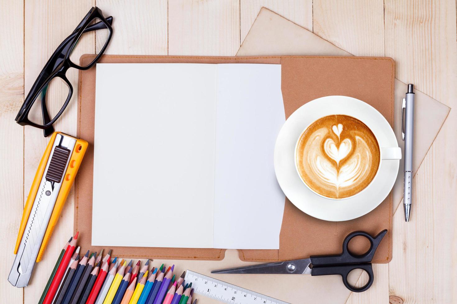 An open blank notebook with colour pencils, pens and cup of coffee on wooden table photo