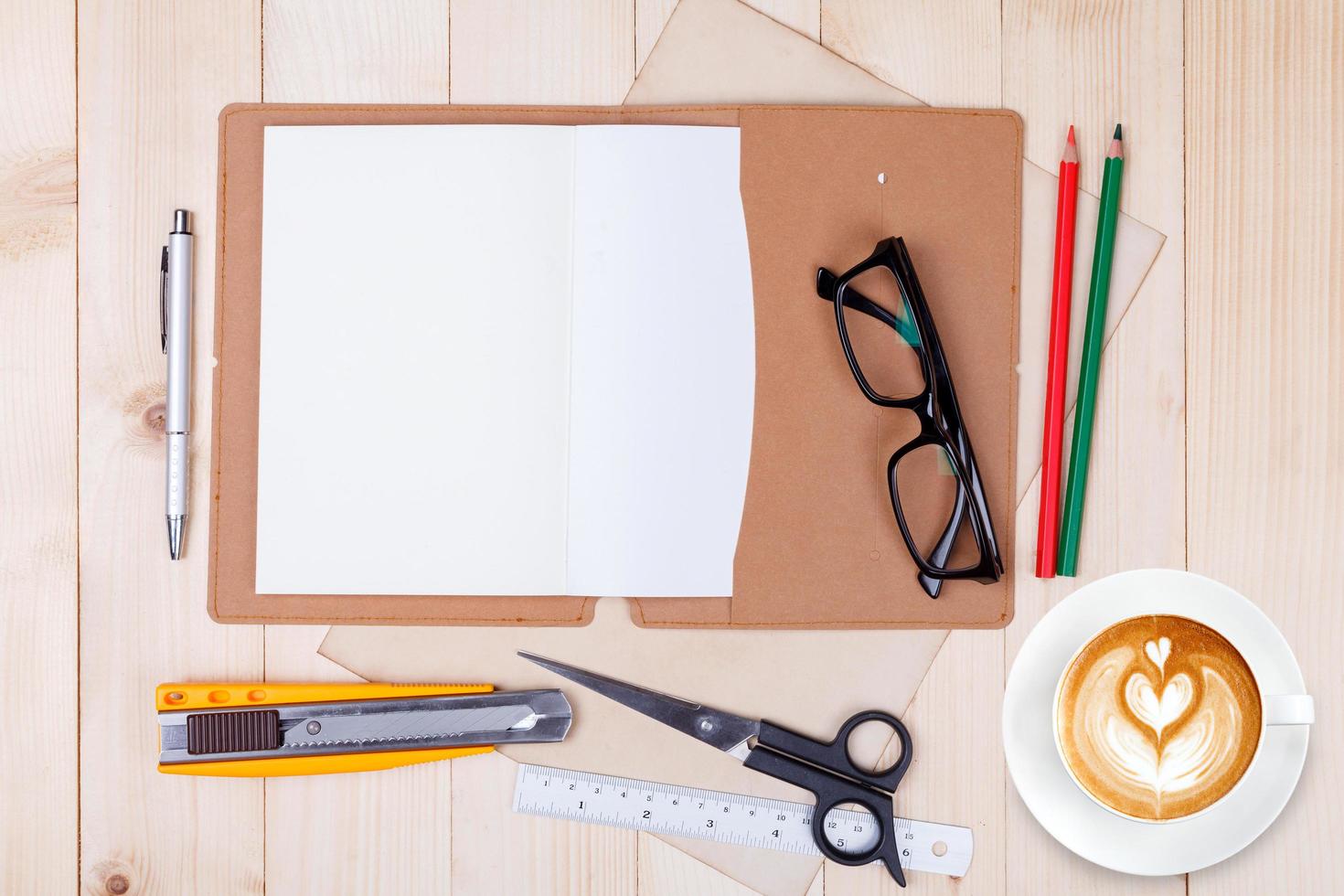 An open blank notebook with colour pencils, pens and cup of coffee on wooden table photo