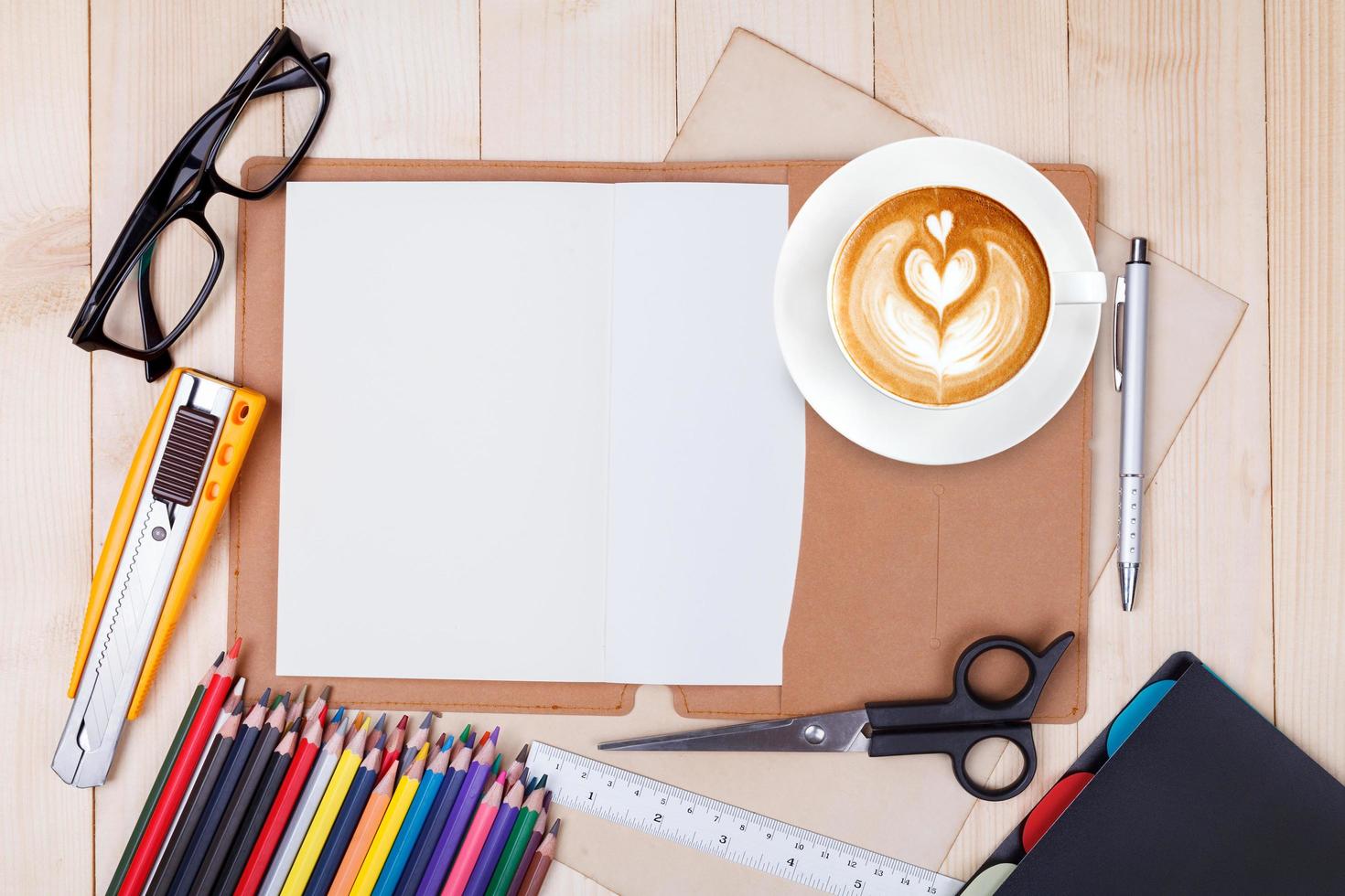An open blank notebook with colour pencils, pens and cup of coffee on wooden table photo