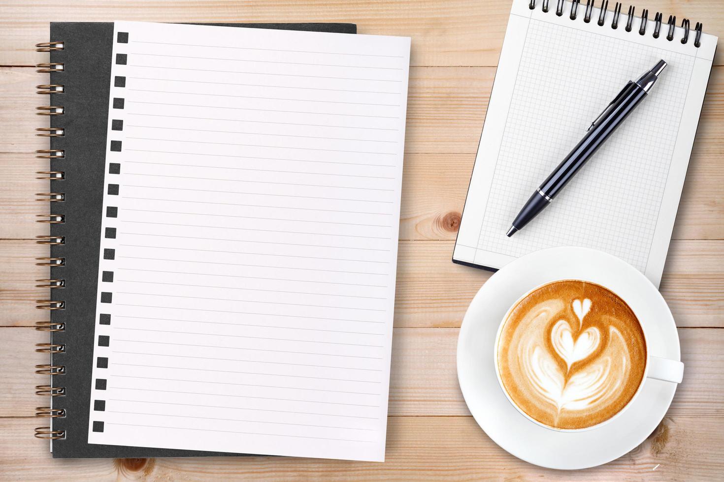 An open blank notebook with pencil and a cup of coffee on wooden table. Latte art coffee on top photo