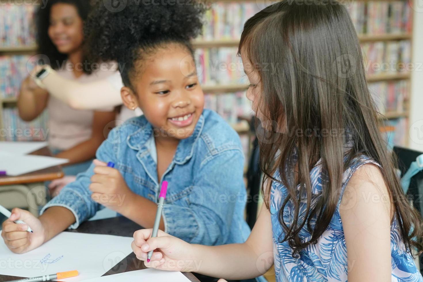 Preschool Girl Kid Drawing With Color Pencil On White Paper On Table In Classroom With Friends photo