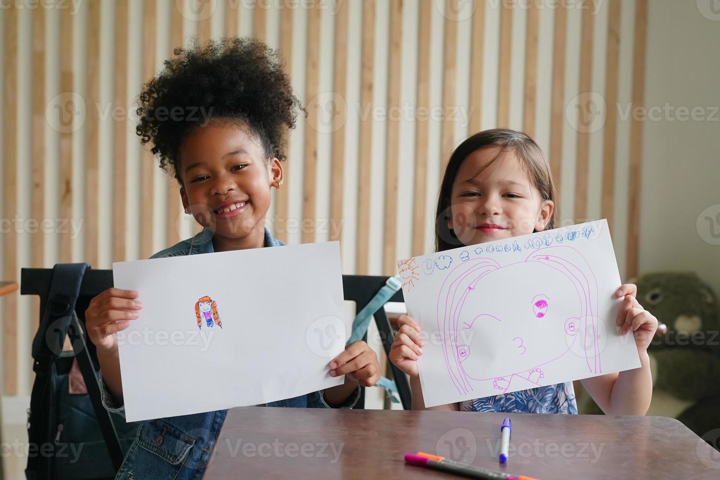 Preschool Girl Kid Drawing With Color Pencil On White Paper On Table In Classroom With Friends photo